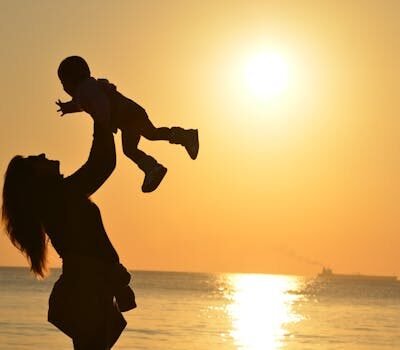 Silhouette of a mother lifting her child at a sunset beach, capturing warmth and love.
