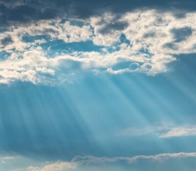 Vibrant sunrays pierce through a cloudy sky, creating a dramatic and dreamy cloudscape.