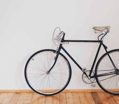 A vintage-style bicycle leaning against a clean white wall with wooden flooring, emphasizing minimalist design.