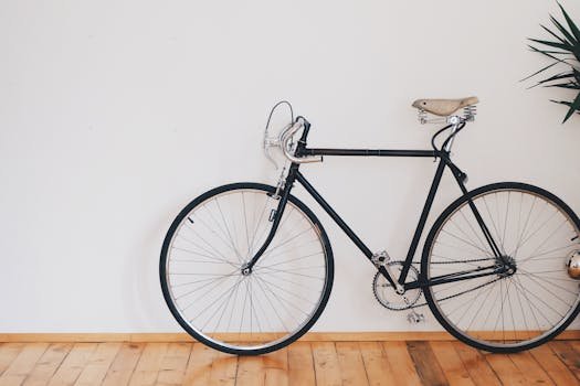 A vintage-style bicycle leaning against a clean white wall with wooden flooring, emphasizing minimalist design.