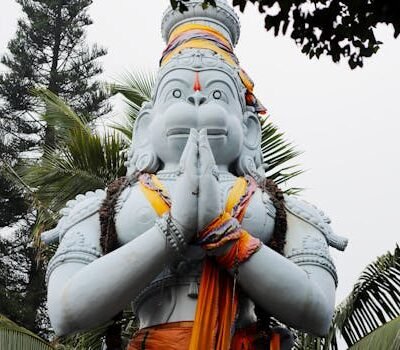 Impressive sculpture of Hanuman with palms, located outdoors among lush greenery.